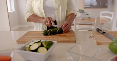 Person Chopping Fresh Zucchini on Wooden Cutting Board in Kitchen
