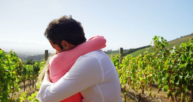Couple embracing in lush vineyard on sunny day. Ideal for concepts of love, romance, togetherness, and serene outdoor leisure. Suitable for use in lifestyle blogs, advertisements for travel and romance destinations, greeting cards, and campaigns promoting countryside retreats.