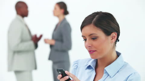 Businesswoman Smiling at Phone with Colleagues in Background
