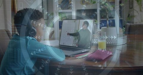 Young boy wearing headset studying online at home table with laptop, notebooks, pencils