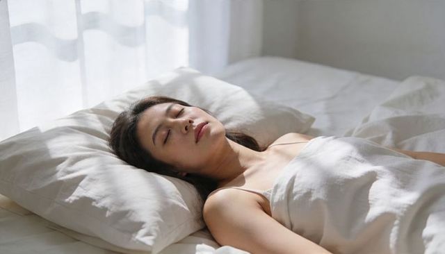 Sunlit woman sleeping peacefully on white bed linen for sleep and minimalist lifestyle