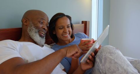 Relaxed african american couple smiling with tablet in bedroom