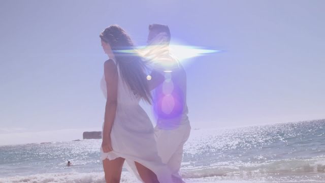 Couple walking along a beach with light flare creating a magical effect. Ideal for vacation advertisements, honeymoon packages, romantic getaways, and summer holiday promotions.