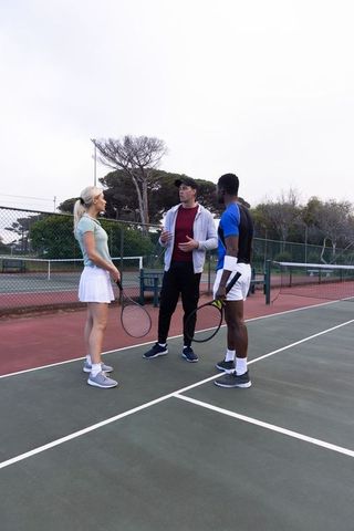 Tennis coach giving tactical instruction to mixed-gender players on outdoor hard court