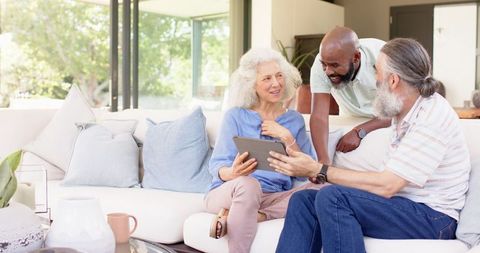 Senior Friends Using Tablet and Laughing Together in Modern Living Room