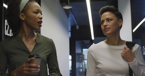 Two professionals talking while walking in modern office corridor with coffee
