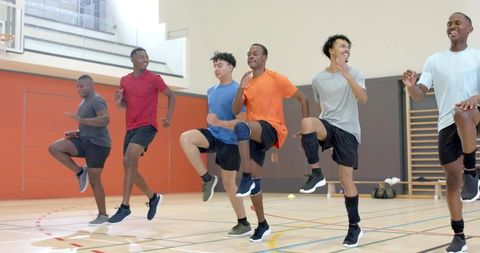 Multiracial male athletes doing high-knee warmup drill in indoor sports court