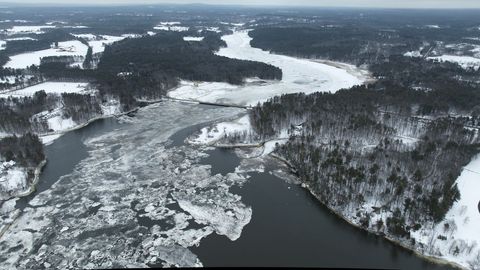 Aerial winter landscape showing river ice breakup and snow-covered shoreline with bridge