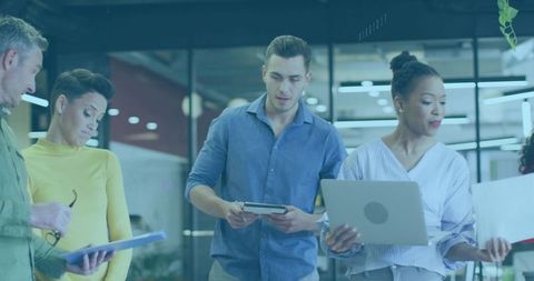 Diverse team collaborating around laptops and documents in modern glass-walled office