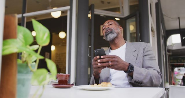 Middle-aged man enjoying coffee while scrolling phone at outdoor cafe - Download Free Stock Images Pikwizard.com