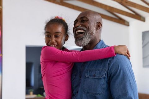 African american grandfather and granddaughter laughing and hugging at home family bonding