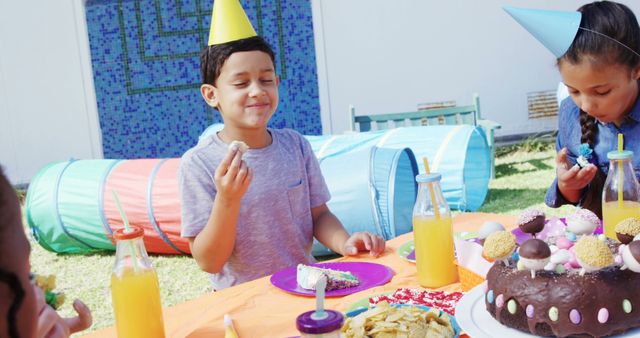 A young boy of Asian ethnicity celebrates at an outdoor birthday party, with copy space. Festive decorations, snacks, and a cake on the table contribute to the cheerful atmosphere.