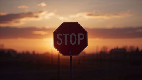 Stop sign silhouetting against warm sunset over rural roadside with rimlight glowing