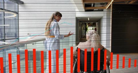 Caregiver guiding older woman in wheelchair through hospital corridor with data overlay