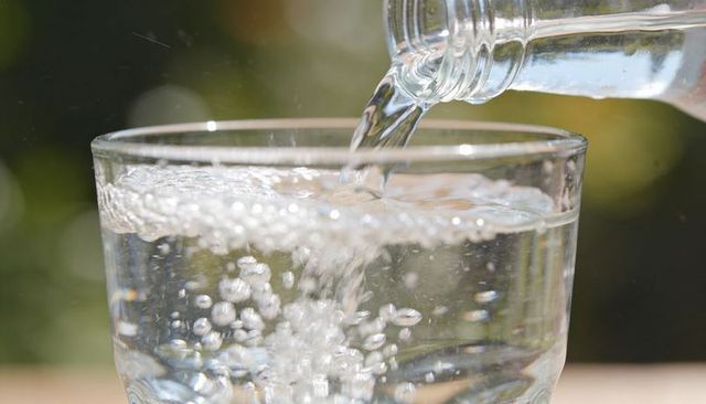 Pouring clear water into glass with sparkling bubbles, sunlight bokeh and outdoor freshness