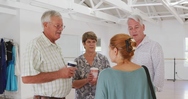 Mature adults chatting and drinking beverages in spacious, well-lit dance studio. Ideal for uses in social interaction concept, community engagement, recreation, lifestyle, leisure activities, and group discussions.