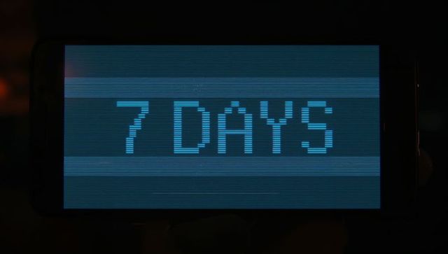 Cyan pixelated countdown display showing 7 days with retro scanlines, dark bezel, thumb silhouettes