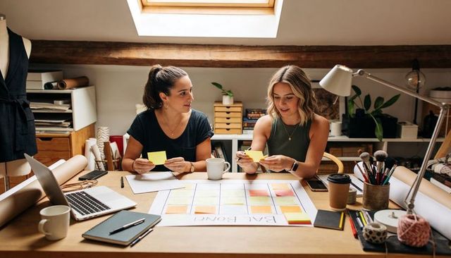 Designers collaborating over sticky note brand board in sunlit loft workspace planning teamwork