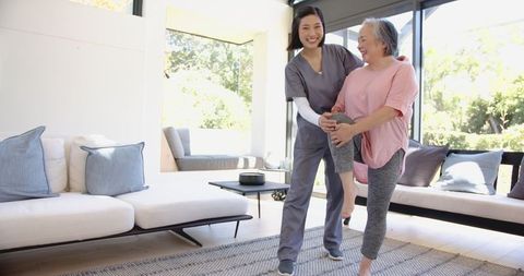 Physiotherapist assisting senior woman with leg exercise at home