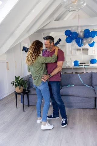 Mature couple embracing and celebrating in bright loft living room with blue balloons