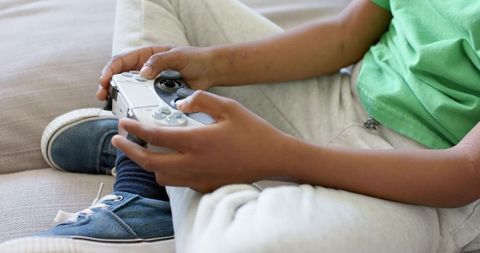 African american child playing console game on couch holding wireless controller close-up