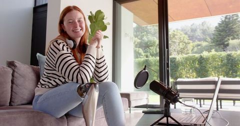 Woman with prosthetic leg streaming in modern home holding plant