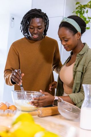 African american couple baking together in bright cozy home kitchen, whisking batter