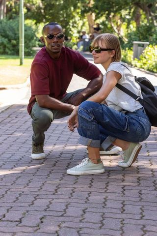 Crouching multiracial couple wearing sunglasses on sunlit park walkway, casual vibe
