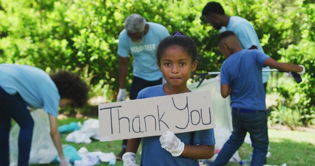 Smiling biracial granddaughter holding thank you sign, clearing up trash outdoors with family. Ecology, volunteering, recycling, nature conservation, family and togetherness.