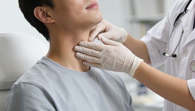 Doctor examining patient neck with gloved hands during throat examination