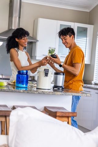 Smiling diverse couple making green smoothie at modern granite kitchen island