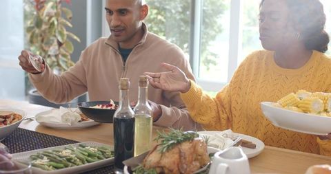 Sunlit family dinner with diverse couple sharing roast chicken, passing corn and sides