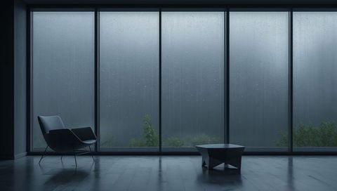 Minimalist living room showing rain-streaked floor-to-ceiling windows and lounge chair