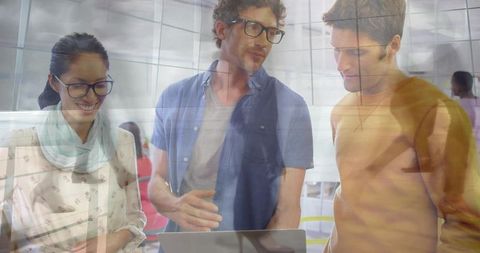 Young professionals collaborating over laptop in modern glass office with reflections