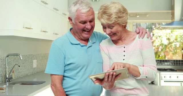 Senior couple enjoying time together, engaging with technology in a bright, modern kitchen. Ideal for topics related to family, healthcare, technology use among seniors, or retirement lifestyle.