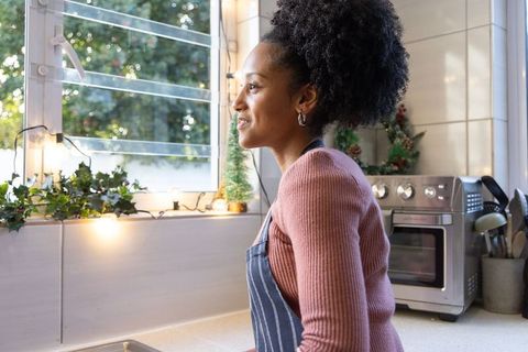 Young african american woman gazing out louvered window in cozy sunlit kitchen