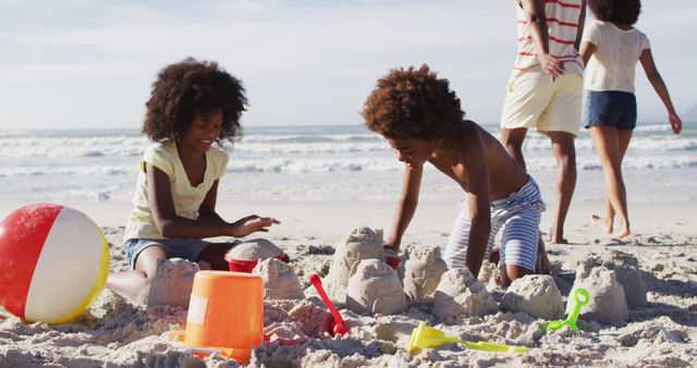 Children enjoying a day at the beach building sandcastles as family members walk along shore in background. Useful for advertising family vacations, summer activities, and beachside resorts. Ideal for promoting outdoor play, bonding time, and holiday experiences.