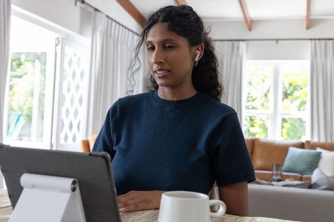 Remote worker using tablet and earbuds at wooden table in bright living room
