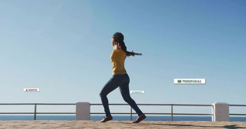 Woman Walking on Sunlit Coastal Promenade in Mustard Top and Jeans Embracing Ocean Breeze