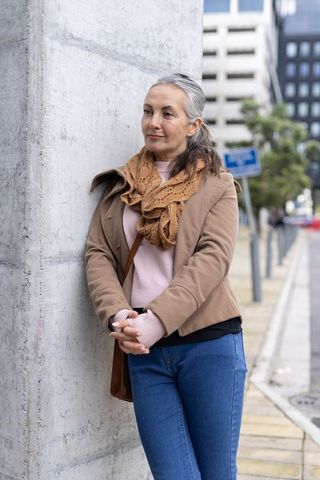Mature woman leaning against concrete column wearing knitted scarf and casual coat