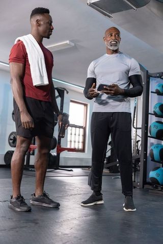 African american trainer coaching client in gym holding tablet and water bottle during workout