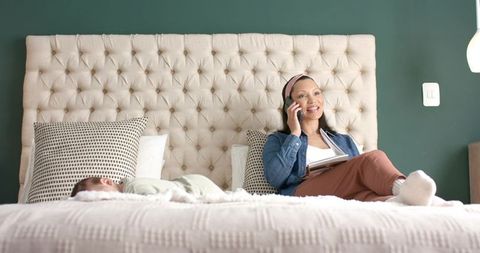 Mother Relaxing on Bed with Infant, Taking Call and Checking Notes