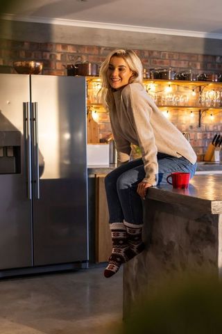 Cozy kitchen scene woman in late 20s sitting on concrete island holding red mug