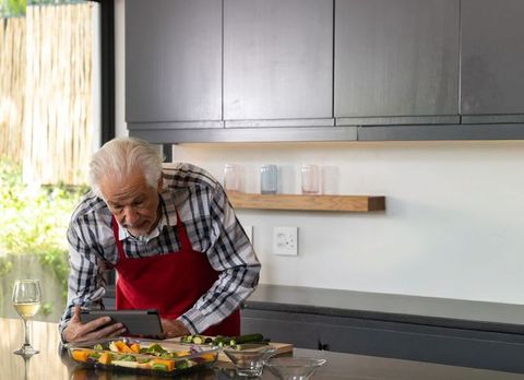 Senior man using tablet while preparing vegetable tray on countertop in modern kitchen