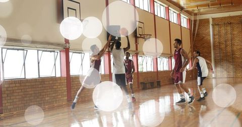 High school basketball players jumping for layup in gymnasium with defender contesting shot