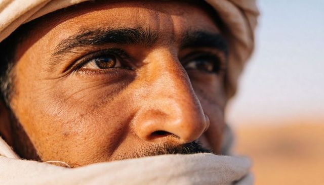 Gazing desert man wearing wrapped headscarf and scarf closeup showing fabric texture
