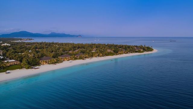 Curving tropical resort peninsula with white sand beach and turquoise lagoon, palm villas