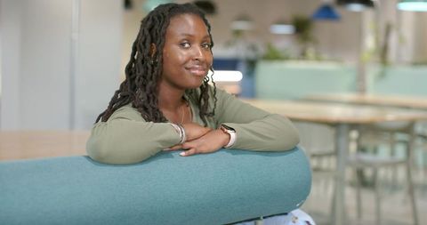 Leaning woman with locs resting on rounded teal backrest in modern pastel coworking lounge