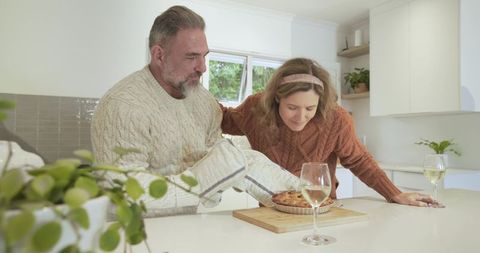 Couple Presenting Homemade Pie on Kitchen Island with Wine Glasses