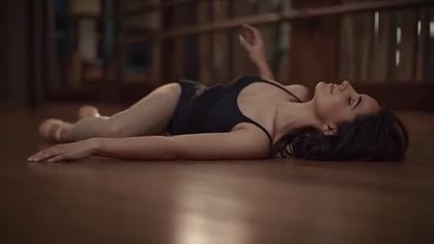 Ballerina Lying and Arching Torso on Studio Floor Wearing Black Leotard and Pointe Shoes
